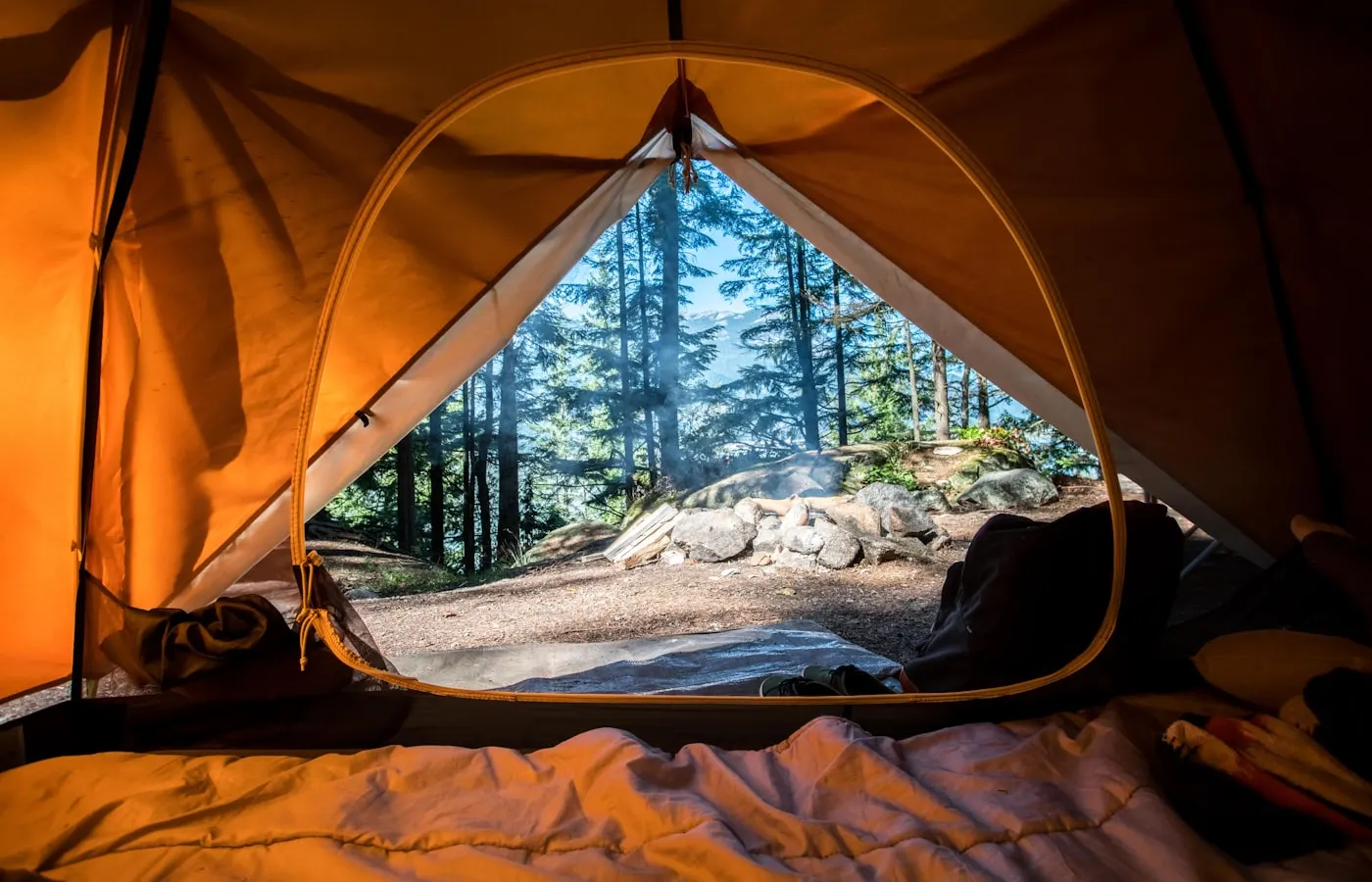 A real campsite view from inside a tent, with warm canvas and trees beyond the campfire.